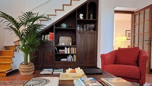 Uma sala de estar acolhedora com escada, estante, poltrona vermelha e mesa de centro com livros e uma planta.