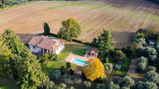 Vista aérea de uma propriedade com um amplo campo, piscina e duas casas com telhados de cerâmica.