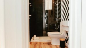 Ein modernes Badezimmer mit Toilette in Weiß, einer Duschkabine aus Glas und einer Wand mit schwarzen Fliesen.
