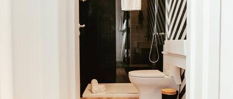 Ein modernes Badezimmer mit Toilette in Weiß, einer Duschkabine aus Glas und einer Wand mit schwarzen Fliesen.