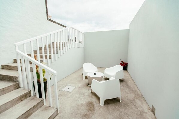 Patio esterno moderno con arredi bianchi, una scala e pavimento in cemento.