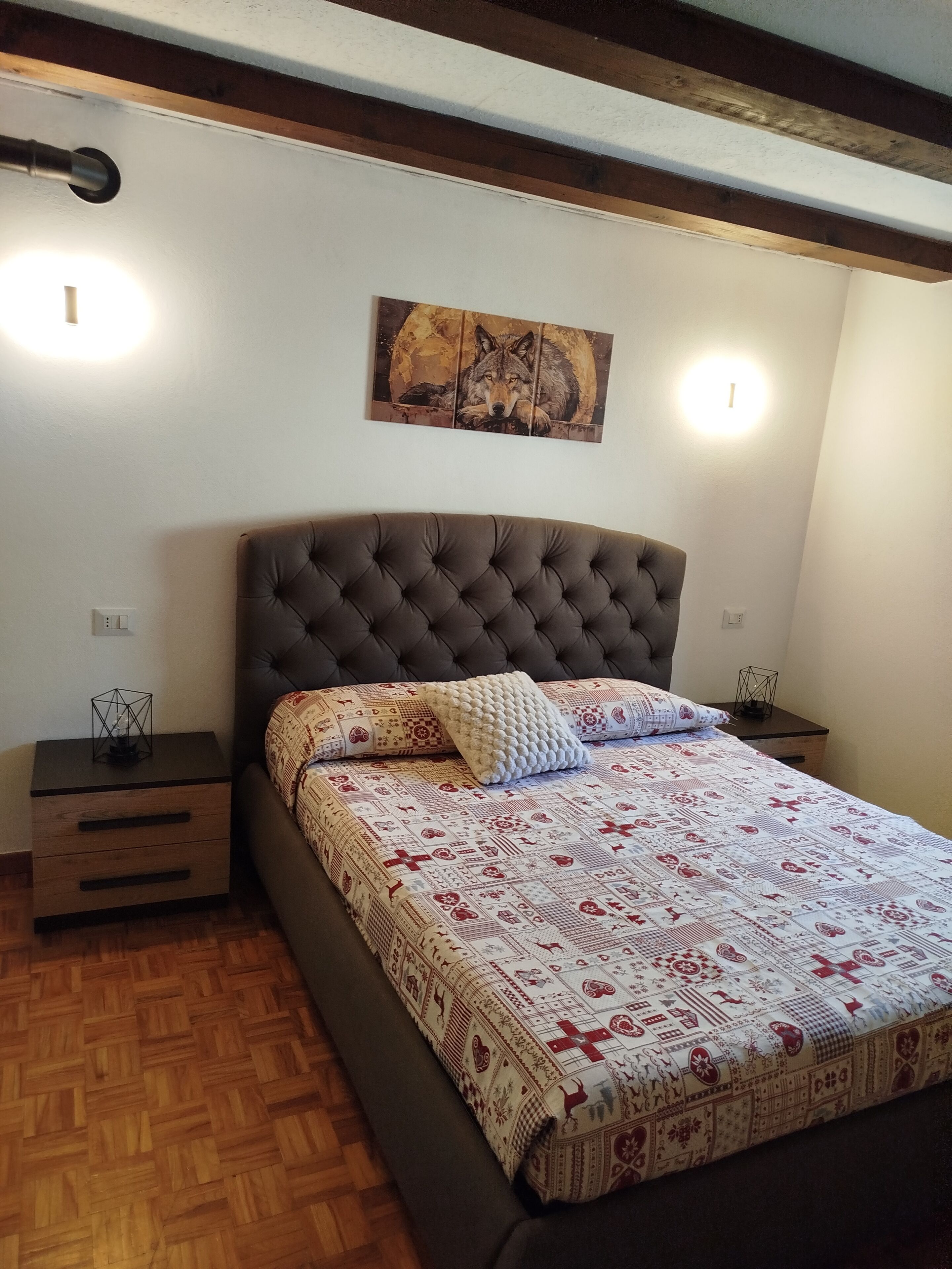 Un dormitorio con cabecera capitonada, colcha estampada, dos mesitas de noche con lámparas y una obra de arte colgada en la pared.
