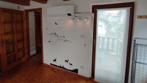 Ein Zimmer mit Holzbalken, einer weißen Wand mit einem Wandbild zum Thema Natur, einer Tür, die nach draußen führt, und einem Fenster mit Blick auf Gebäude.