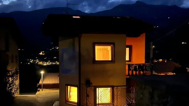 Ein kleines, zweistöckiges Gebäude mit Balkon und Fenster, umgeben von Bergen und einem bewölkten Himmel.