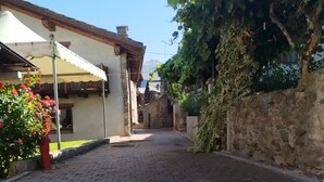 Ein gepflasterter Gang mit Kopfsteinpflastern, gesäumt von Gebäuden mit Steinmauern und einem Holzzaun.