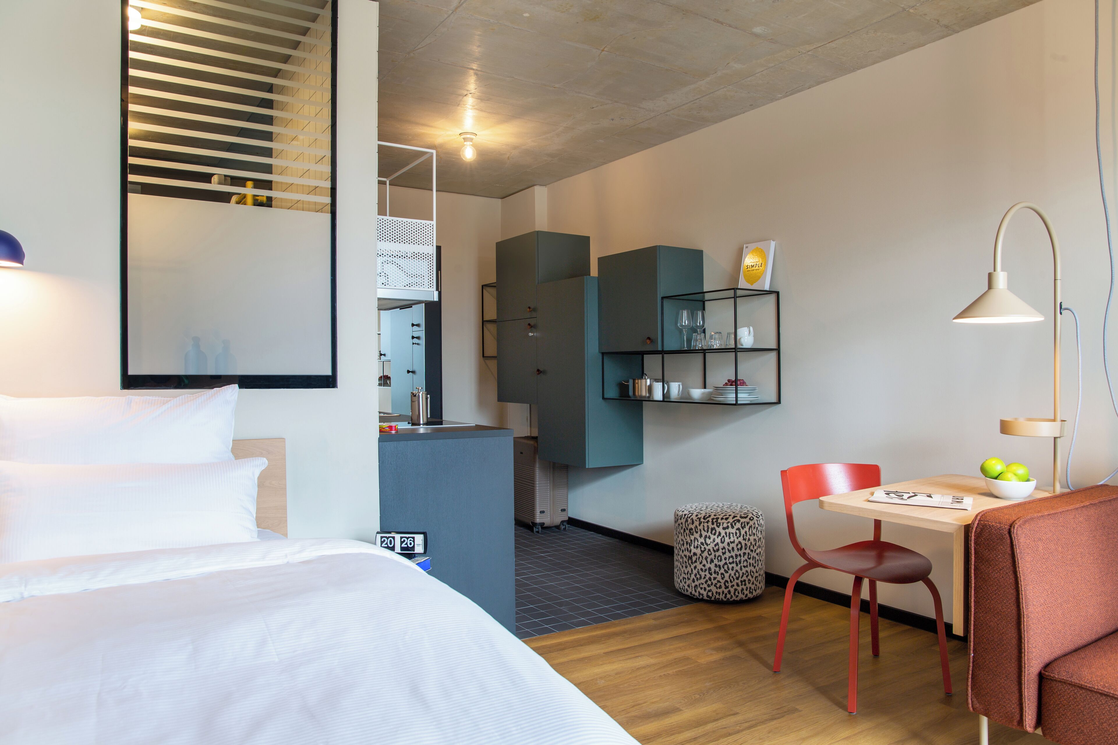 Ett hotellrum med en säng, ett skrivbord, en stol, en lampa och en garderob.