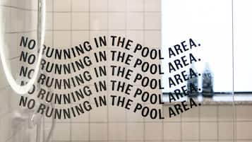 A bathroom with a glass shower enclosure and a tiled wall with a repeated warning sign.