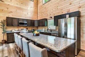 A modern kitchen with granite countertops, stainless steel appliances, and dark wooden cabinetry. - The Mountain Estate by Ghosal Luxury Lodging (Gatlinburg)