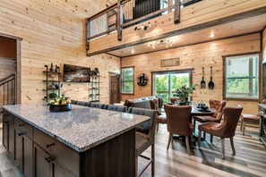 A spacious kitchen with a large island, wooden walls, and a dining area with leather chairs. - The Mountain Estate by Ghosal Luxury Lodging (Gatlinburg)