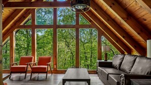 Un ampio loft con soffitto alto, ampie finestre che si affacciano su un lussureggiante verde, un divano in pelle e due poltrone.