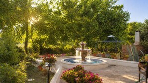 A garden with a fountain, potted plants, and a brick wall. - Lesvos Garden Escape - A Serene Escape in Nature (Vatoussa)