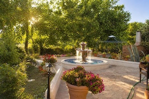Ein Garten mit Brunnen, Blumentöpfen und einer Ziegelmauer.