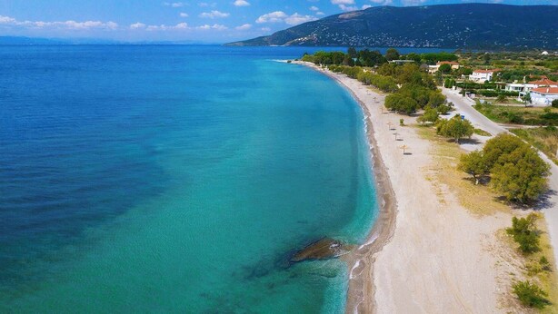 A coastal area with a sandy beach, clear turquoise waters, and a road lined with trees and buildings. - Lesvos Garden Escape - A Serene Escape in Nature (Vatoussa)
