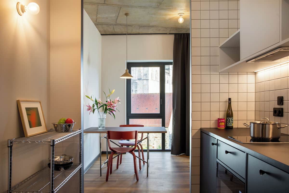 A modern kitchen with a dining area, featuring a table, chairs, a vase with flowers, and a bottle on the counter.