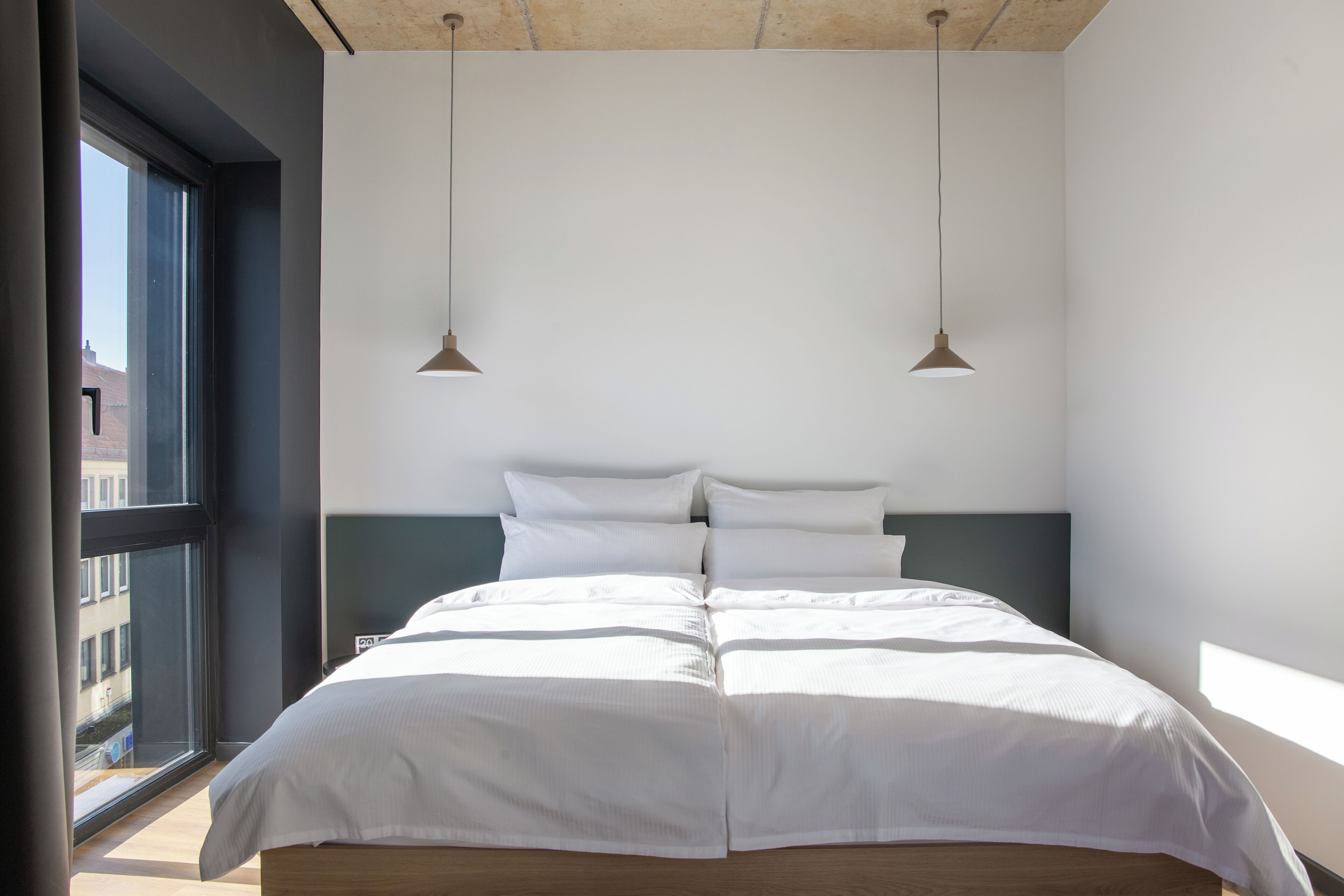 Un dormitorio moderno con una cama grande, dos lámparas colgantes y vistas por una ventana.