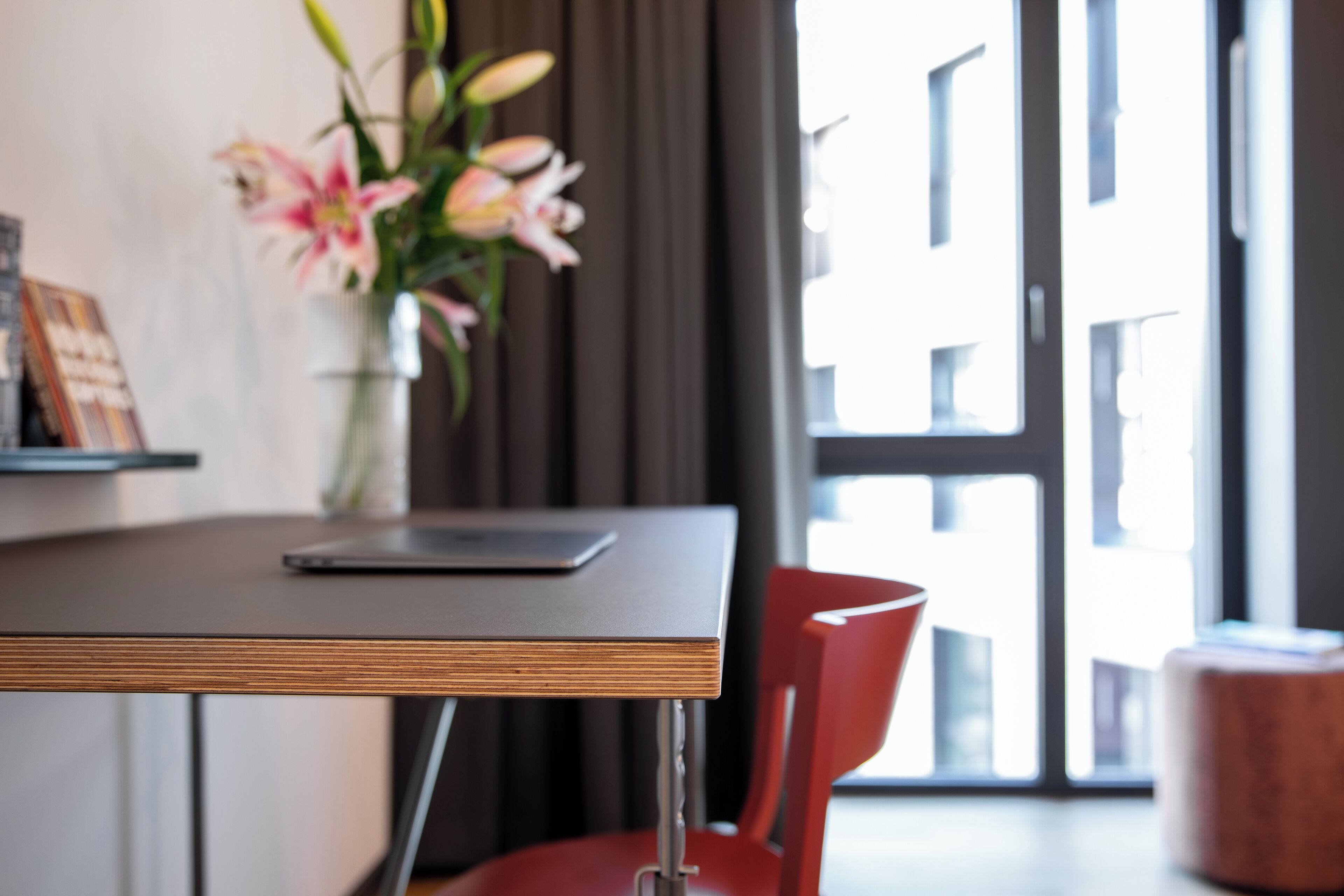A modern dining area with a wooden table, a red chair, and a vase with flowers.