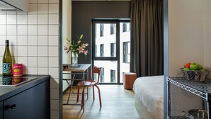 Camera d'albergo compatta con angolo cottura, zona pranzo, un letto e vista sulla città da una grande finestra.