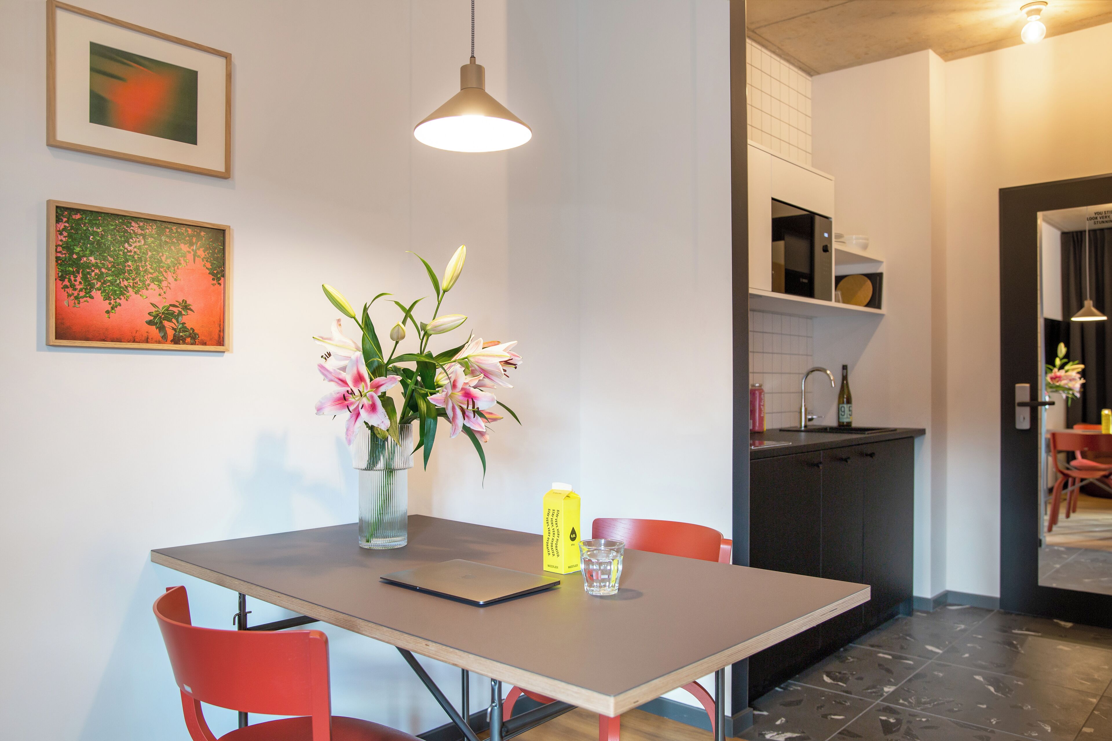 A modern kitchen with a dining table, chairs, and a vase of flowers.
