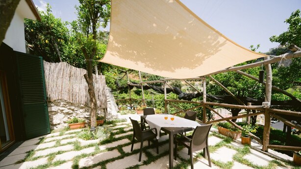 Eine Terrasse im Freien mit Tisch und Stühlen, umgeben von einem Holzzaun und Kübelpflanzen.