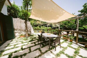 Um pátio externo com uma mesa e cadeiras, cercado por um cercado de madeira e plantas em vasos.