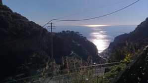 Eine Küstenlandschaft mit blauem Himmel, sonnenbeschienenem Meer und einer kurvigen Straße durch felsiges Gelände.