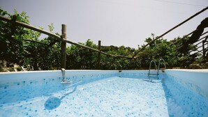 Ein Schwimmbad mit Fliesenboden, umgeben von einem Holzzaun und Grünpflanzen.