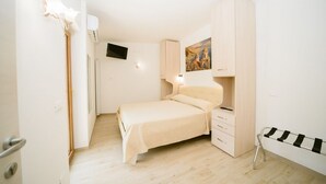 Ein schlicht eingerichtetes Schlafzimmer mit Bett, Kleiderschrank, Fernseher und einem Bild an der Wand.