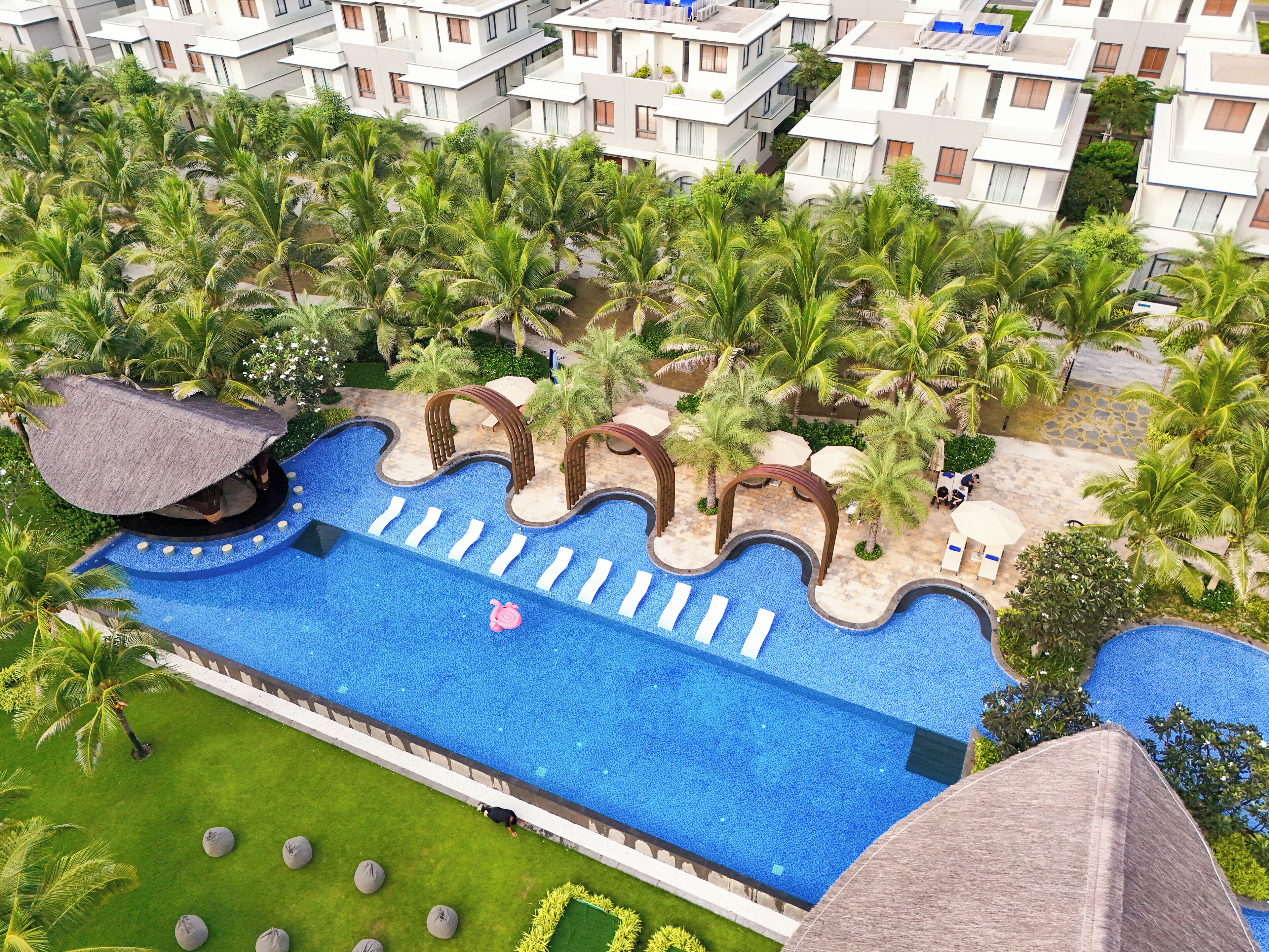 Eine Luftaufnahme eines Resorts mit großem Schwimmbecken, Palmen und modernen Gebäuden.
