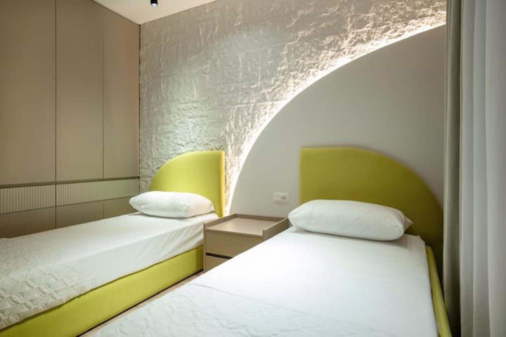 A modern hotel room with two single beds, each with a yellow headboard and white bedding.