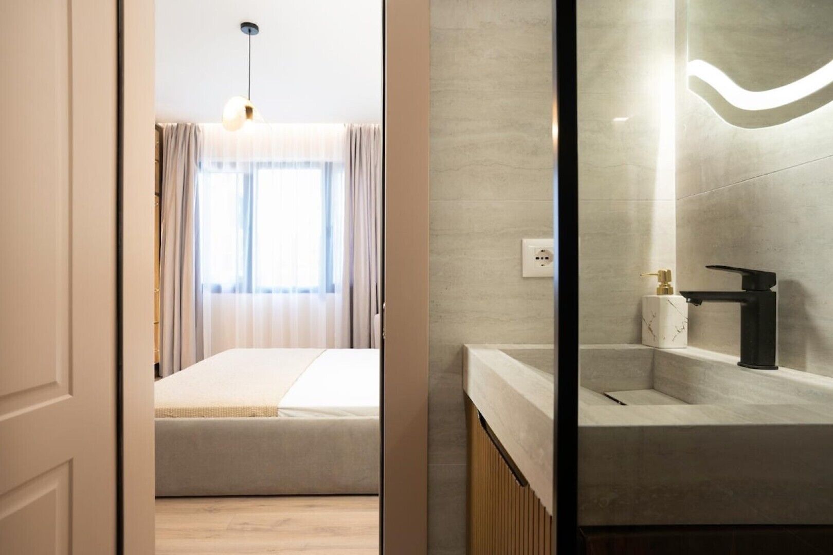 Una habitación de hotel moderna con cama, baño con encimera de mármol e iluminación colgante.
