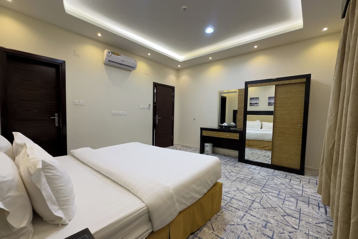 A hotel room with a bed, a desk, a mirror, and an air conditioning unit.