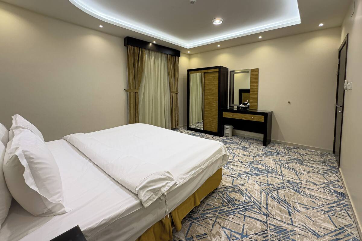 A hotel room with a neatly made bed, a large mirror, a vanity with a sink, and a patterned carpet.