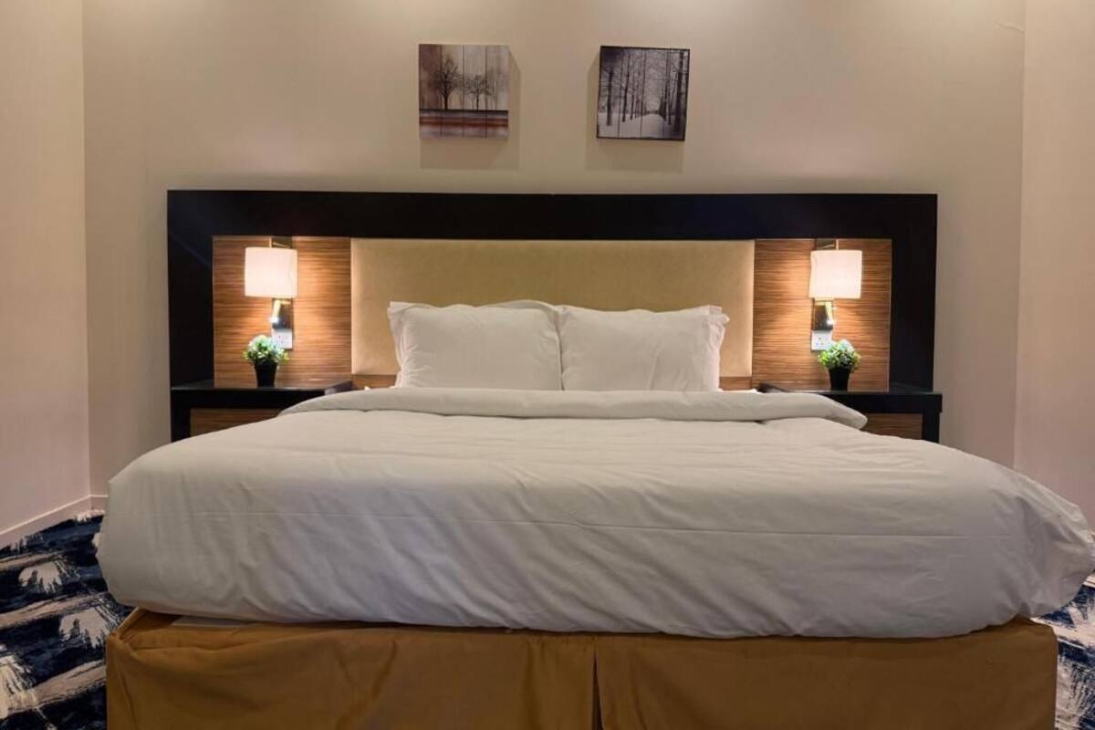 A neatly made bed with white linens, two bedside lamps, and a headboard with a wooden panel design.