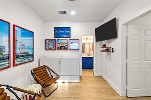 A hallway with a white door, a mounted TV, and framed pictures on the wall. - Beach House | Swim Spa, Hot Tub, Mini Golf, Games (Galveston)