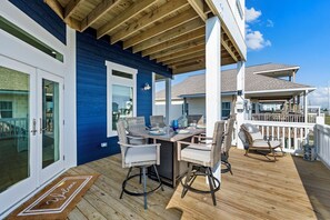 A deck with a table and chairs, a welcome mat, and a view of the ocean. - Beach House | Swim Spa, Hot Tub, Mini Golf, Games (Galveston)