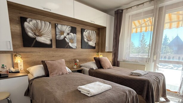Ein Hotelzimmer mit zwei Betten, einem Holzkopfteil, Wandbildern, Nachttischlampen und Blick ins Freie.