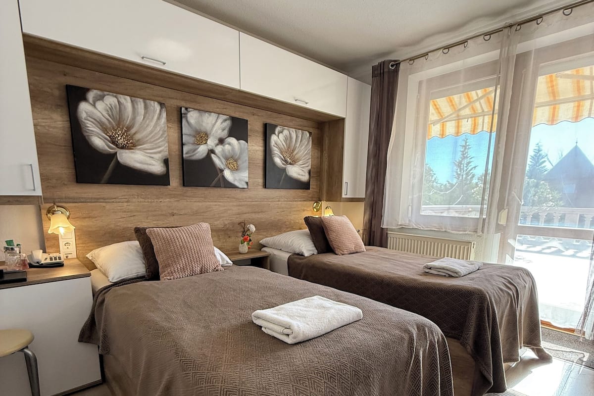 Ein Hotelzimmer mit zwei Betten, einem Holzkopfteil, Wandbildern, Nachttischlampen und Blick ins Freie.