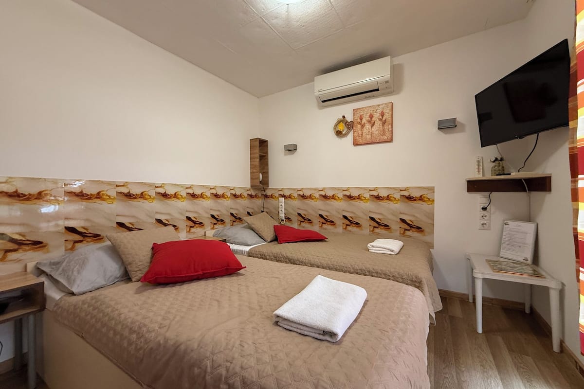 Ein Hotelzimmer mit zwei Betten, einem Fernseher, einer Klimaanlage und einem kleinen Schreibtisch mit Stuhl.