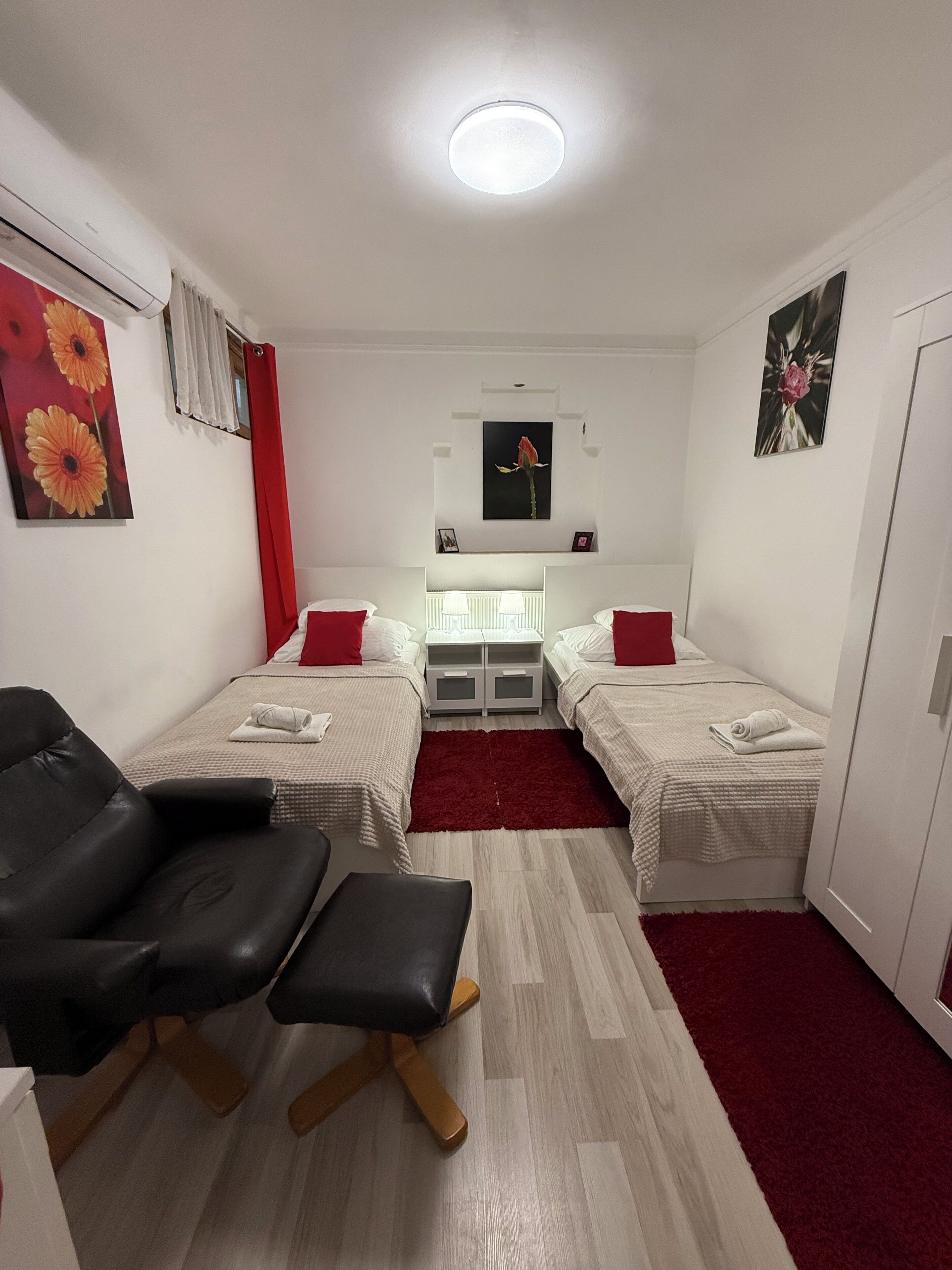 A small, well-lit room with two beds, a desk, and a chair.
