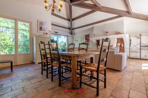 A dining area with a wooden table and chairs, a chandelier, and a view of greenery outside. - Villa Quercia - Valbonne (Valbonne)