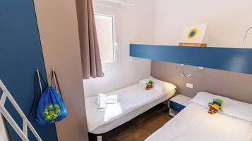 A hotel room with two single beds, a window with curtains, a bedside table with a lamp, and a wall-mounted artwork.