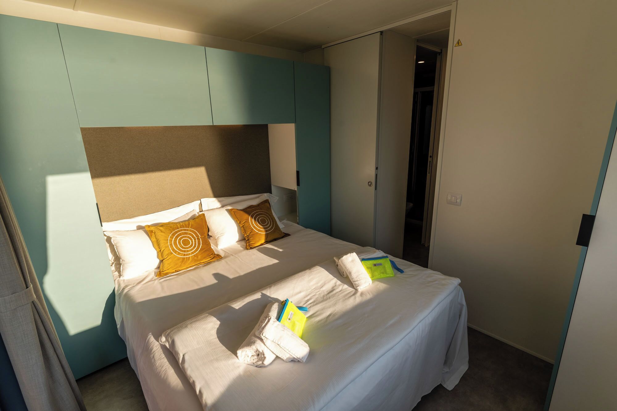 Habitació d'hotel amb un llit, almoines, una tauleta de nit i una porta.