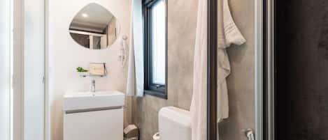Un baño con lavamanos, espejo, toallero y ducha.