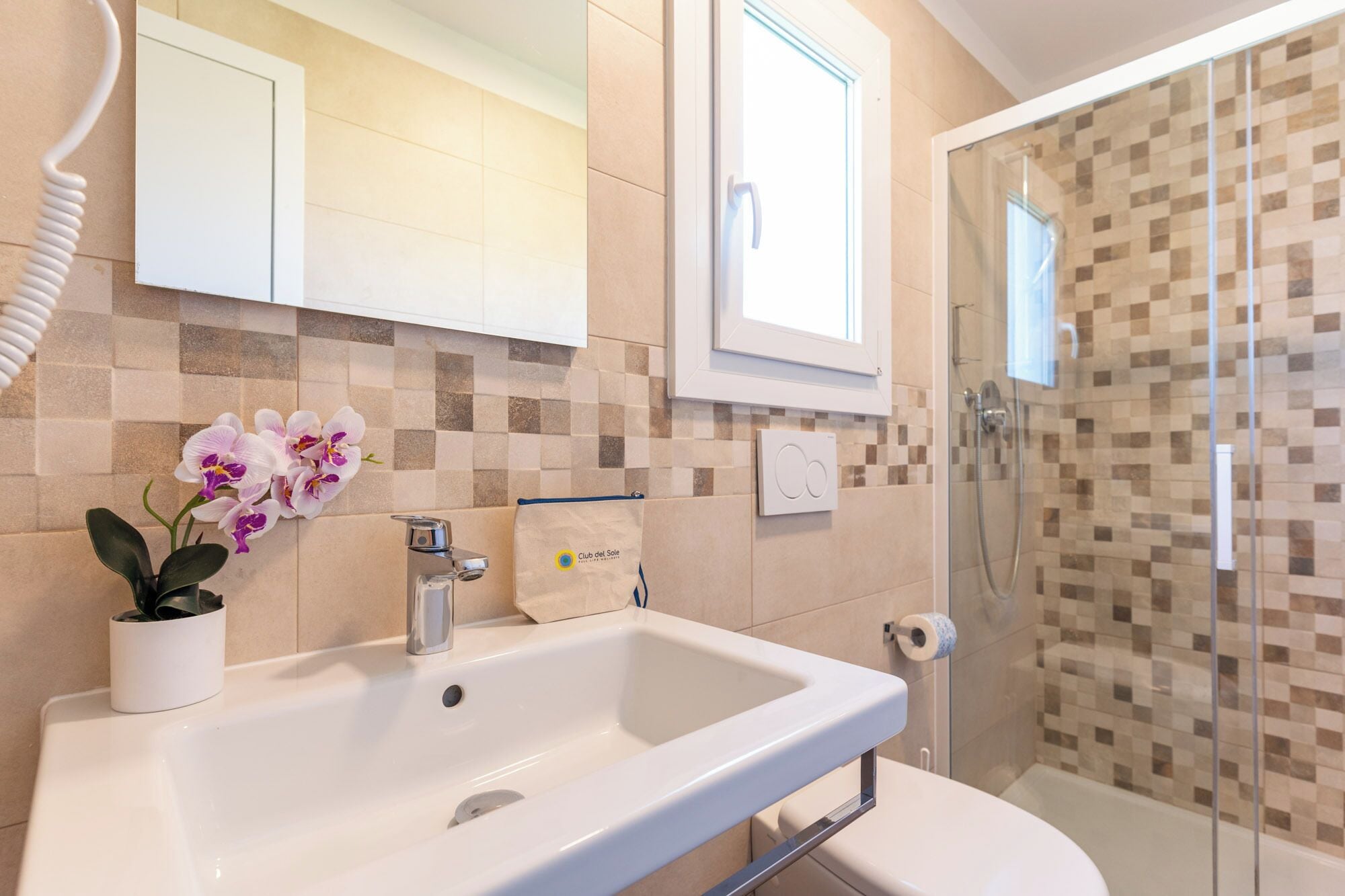 Un baño con lavamanos blanco, cabina de ducha con mampara de vidrio y pared de azulejos.