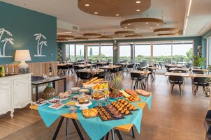 Un'ampia sala da pranzo con numerosi tavoli, un buffet ricco di cibi diversi e grandi finestre che offrono vista sull'esterno.