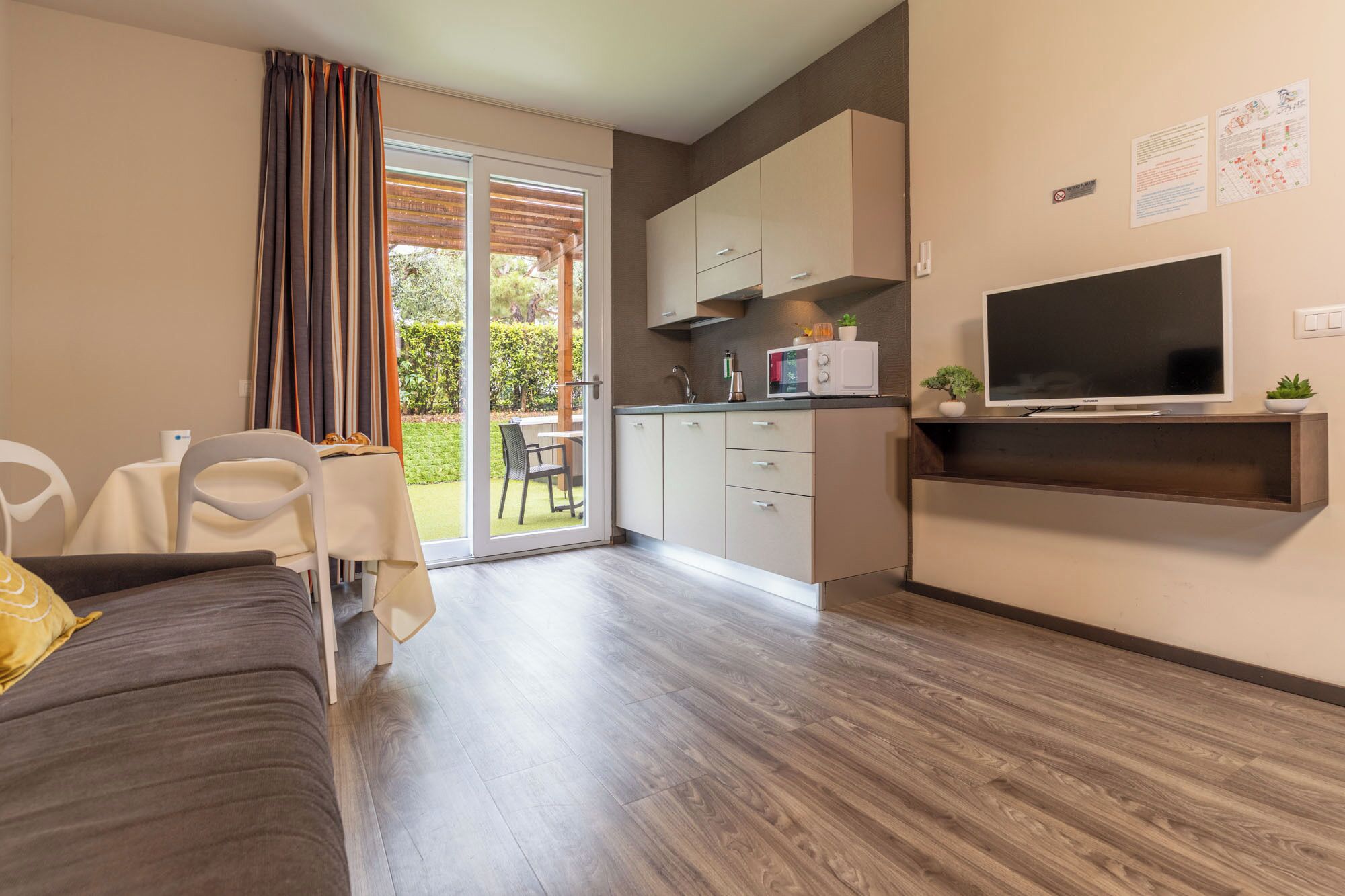 A modern living room with a sofa, a dining table, and a kitchen area with cabinets and a TV.