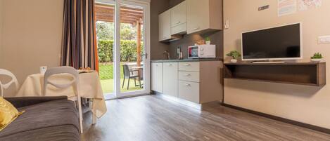 A modern living room with a sofa, a dining table, and a kitchen area with cabinets and a TV.