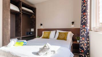 A hotel room with a bed, a wardrobe, a nightstand, a lamp, and a window with curtains.
