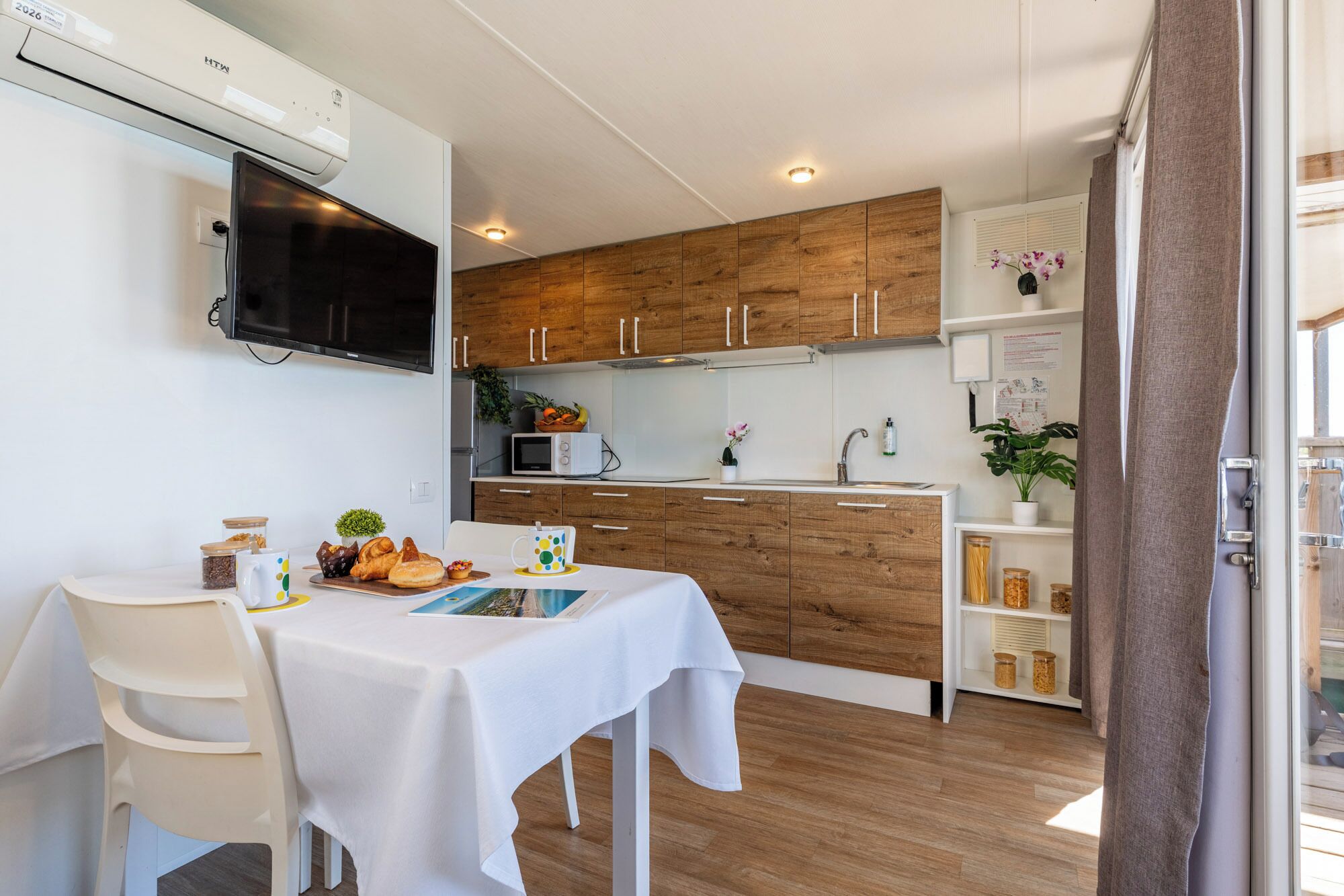 Een moderne keuken met houten kastjes, een magnetron, en een eethoek met een tafel gedekt voor twee personen.