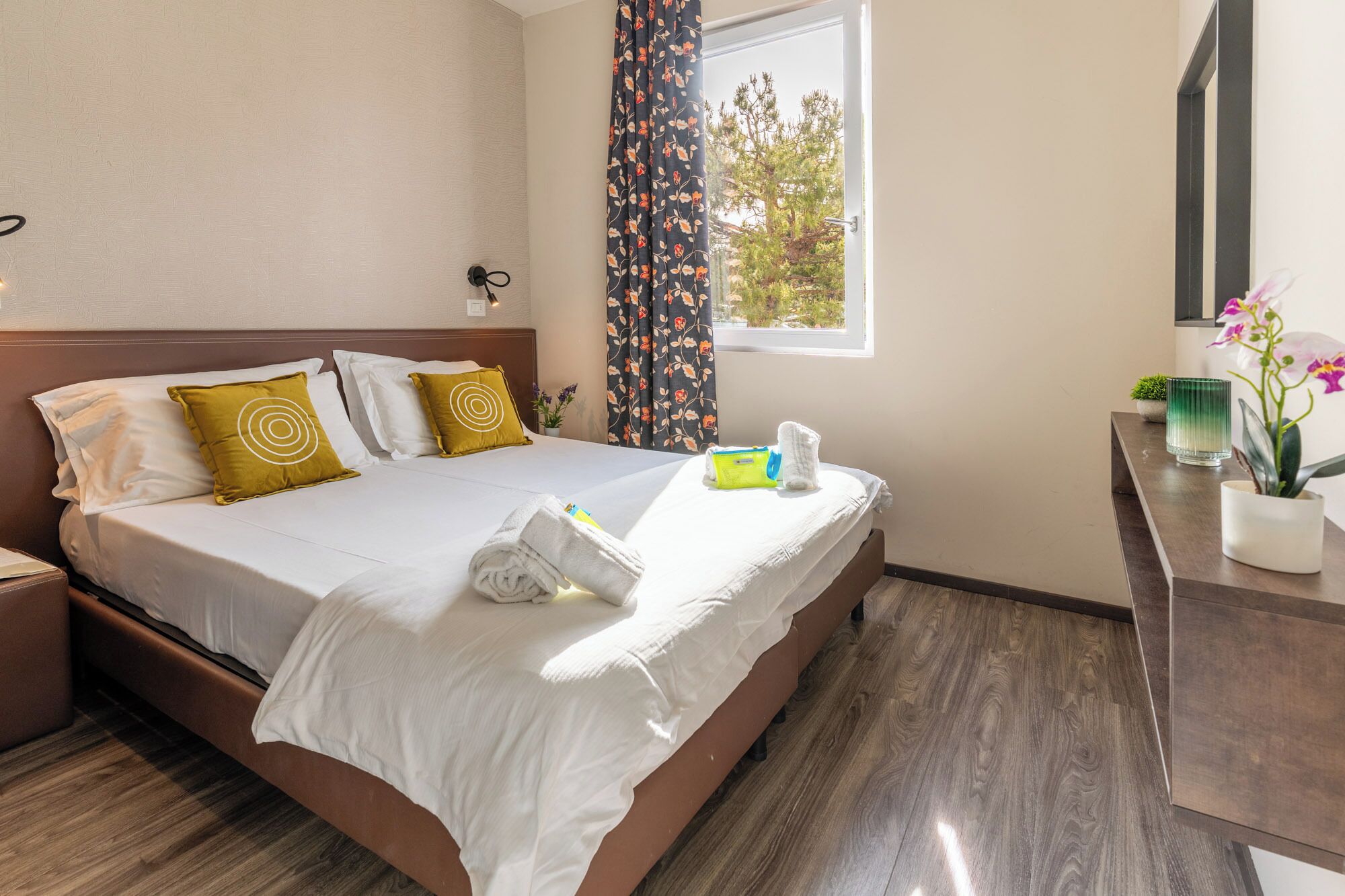 Une chambre d’hôtel avec un lit, une table de chevet, un bureau et une fenêtre avec des rideaux.
